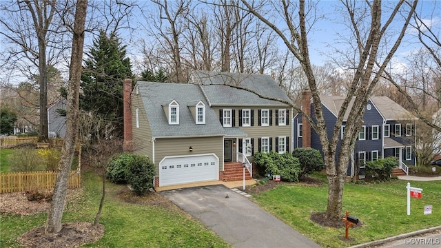 colonial-style house featuring an attached garage, fence, a front yard, a chimney, and driveway