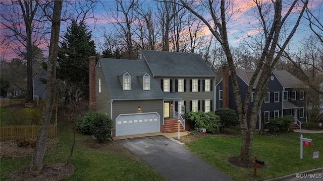 view of front facade featuring driveway, a chimney, an attached garage, and a front yard