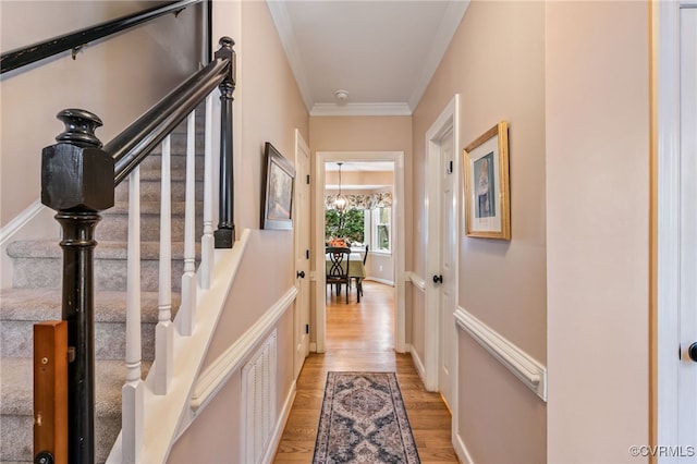 corridor featuring light wood finished floors, visible vents, stairway, and crown molding