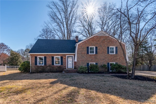 split level home featuring fence, a gambrel roof, a chimney, a front lawn, and brick siding