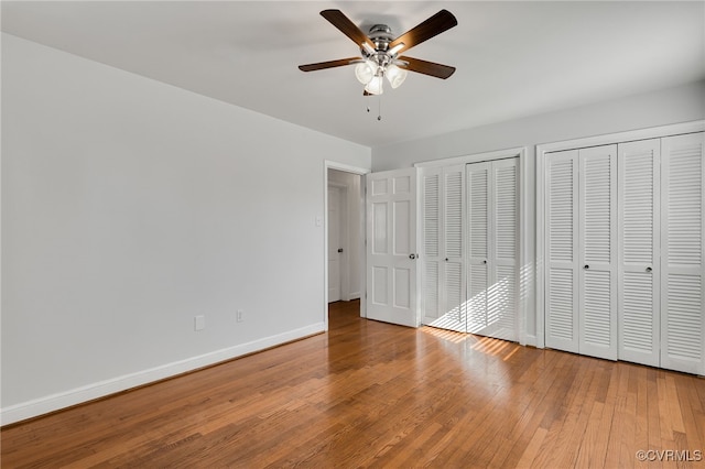 unfurnished bedroom with ceiling fan, two closets, baseboards, and hardwood / wood-style flooring