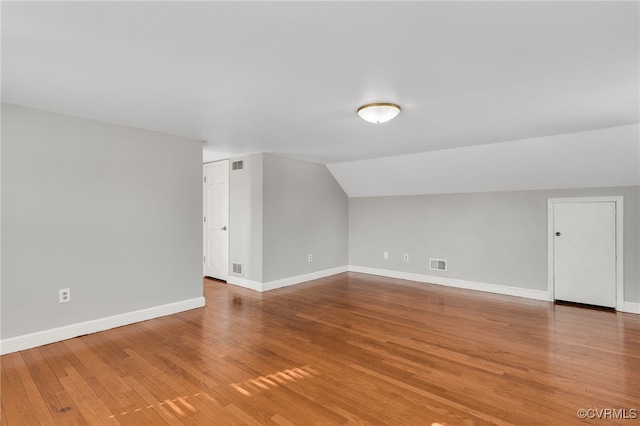 additional living space with visible vents, baseboards, wood finished floors, and vaulted ceiling