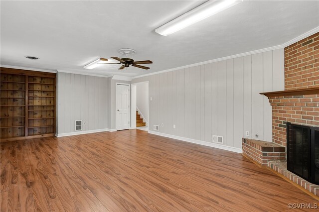 unfurnished living room with stairway, wood finished floors, a fireplace, and ornamental molding