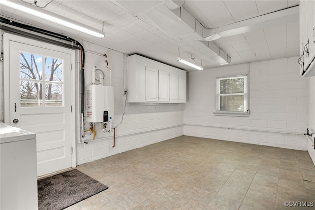 below grade area featuring washer / dryer, concrete block wall, light floors, and tankless water heater