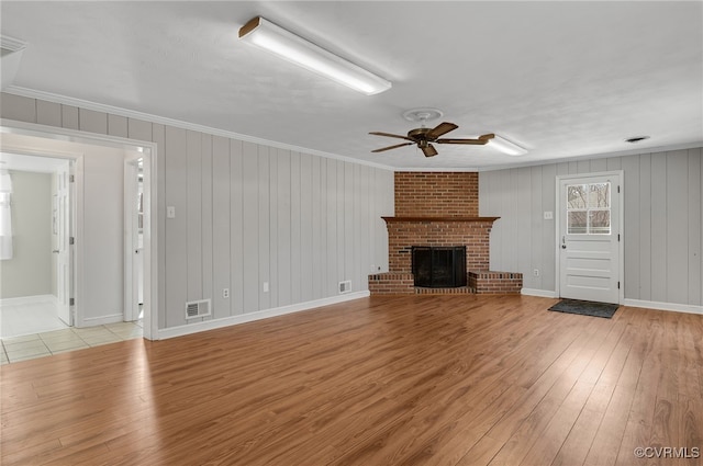 unfurnished living room featuring a brick fireplace, light wood-style floors, visible vents, and ornamental molding