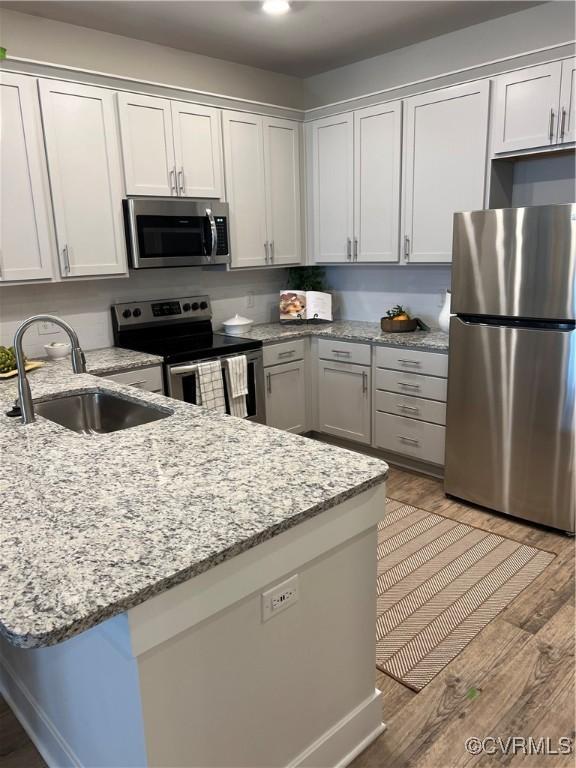 kitchen featuring light wood finished floors, light stone countertops, appliances with stainless steel finishes, a peninsula, and a sink