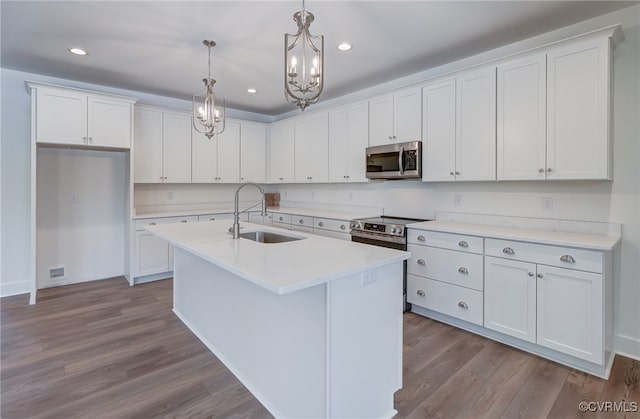 kitchen featuring dark wood finished floors, appliances with stainless steel finishes, hanging light fixtures, white cabinetry, and a sink