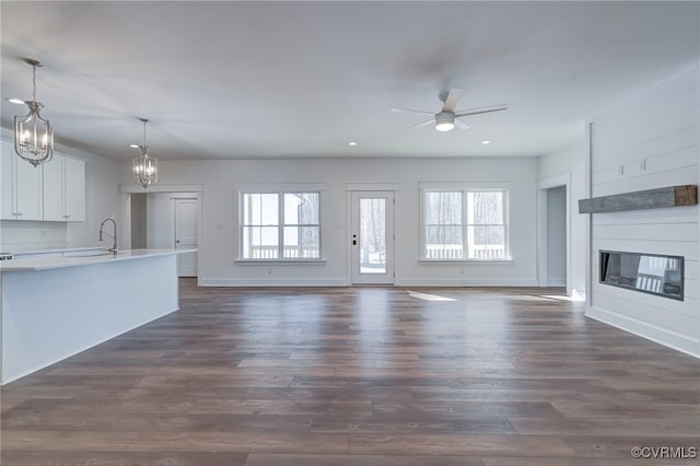 unfurnished living room with a large fireplace, a healthy amount of sunlight, dark wood-style floors, and ceiling fan with notable chandelier