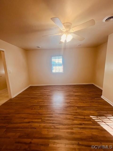 empty room with ceiling fan, visible vents, baseboards, and wood finished floors