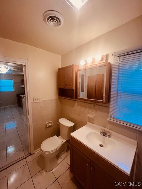 half bath featuring vanity, visible vents, tile patterned flooring, tile walls, and toilet