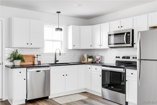 kitchen featuring white cabinetry, dark countertops, appliances with stainless steel finishes, and a sink