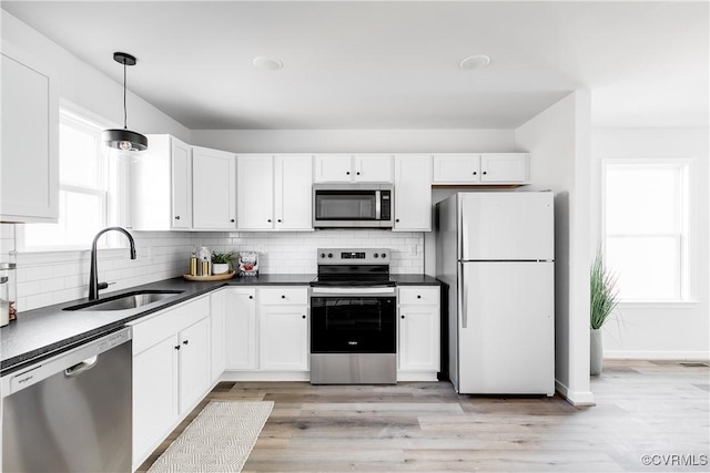 kitchen featuring dark countertops, backsplash, white cabinets, stainless steel appliances, and a sink