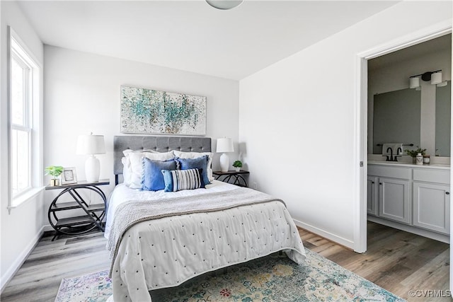 bedroom featuring light wood-style flooring, connected bathroom, baseboards, and a sink