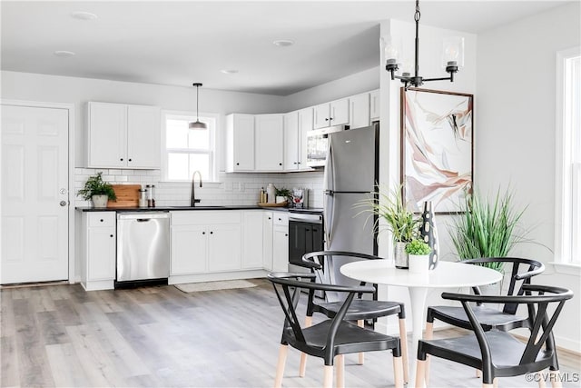 kitchen with light wood-style flooring, a sink, appliances with stainless steel finishes, dark countertops, and tasteful backsplash