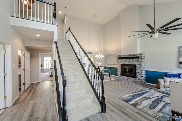 stairs featuring ceiling fan with notable chandelier, a fireplace, high vaulted ceiling, and wood finished floors