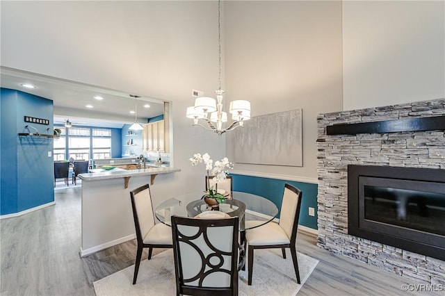 dining area with a stone fireplace, an inviting chandelier, wood finished floors, and a towering ceiling