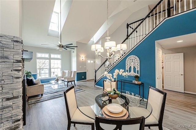 dining room featuring a high ceiling, wood finished floors, stairs, and ceiling fan with notable chandelier