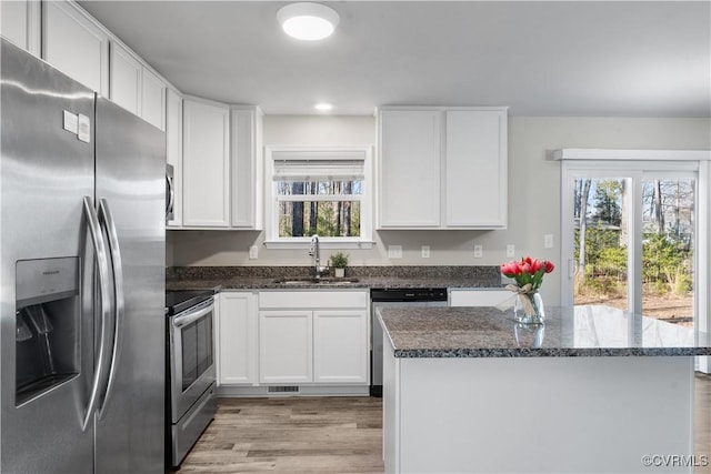 kitchen featuring dark stone countertops, plenty of natural light, appliances with stainless steel finishes, and a sink