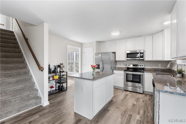 kitchen with a sink, appliances with stainless steel finishes, white cabinets, and light wood finished floors