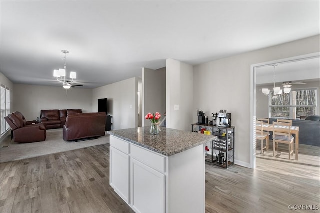 kitchen with ceiling fan with notable chandelier, open floor plan, a center island, white cabinetry, and light wood-style floors