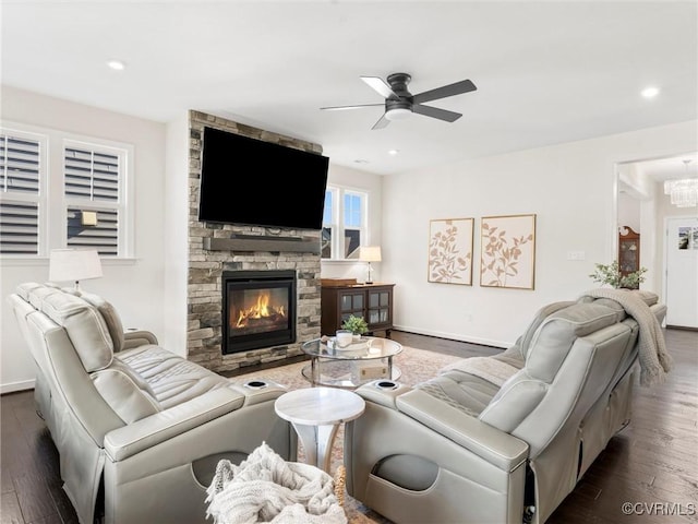 living area with ceiling fan with notable chandelier, wood finished floors, recessed lighting, a stone fireplace, and baseboards