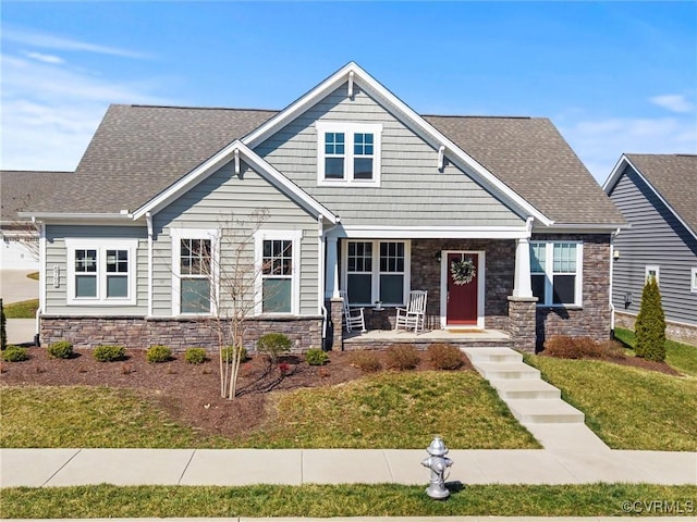 craftsman-style home featuring stone siding, roof with shingles, and a front lawn