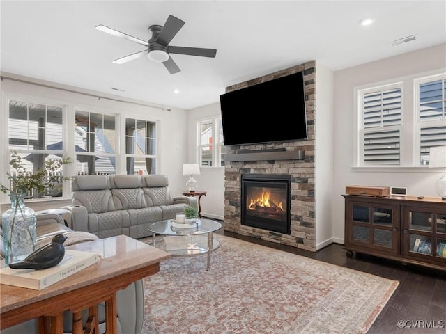 living area featuring visible vents, recessed lighting, ceiling fan, a stone fireplace, and dark wood-type flooring