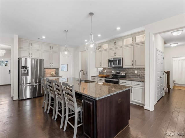 kitchen featuring a center island with sink, a sink, dark wood finished floors, appliances with stainless steel finishes, and a breakfast bar area