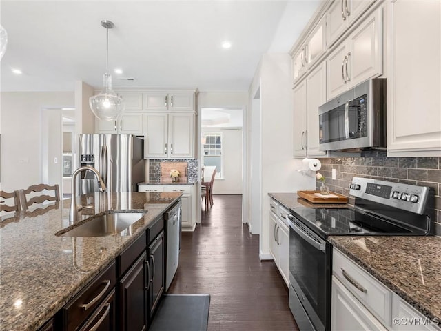 kitchen with dark wood-type flooring, a sink, appliances with stainless steel finishes, white cabinets, and hanging light fixtures