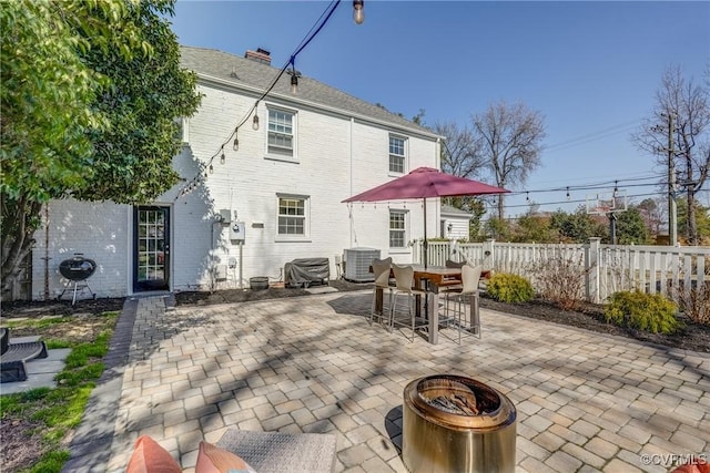 back of house featuring central air condition unit, an outdoor fire pit, fence, brick siding, and a patio area