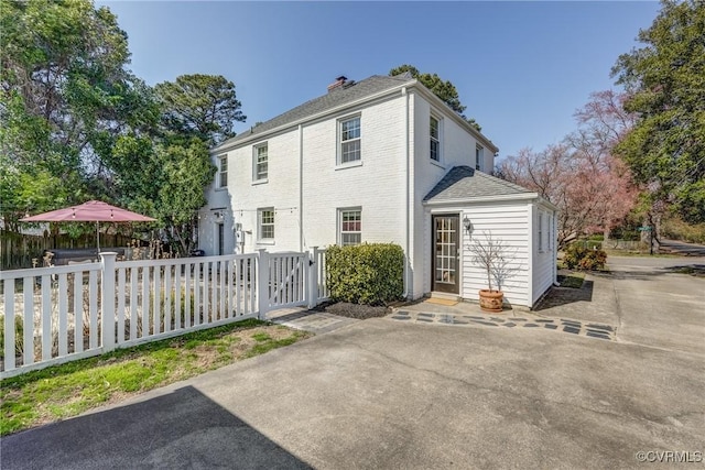 rear view of property with brick siding, a chimney, and fence