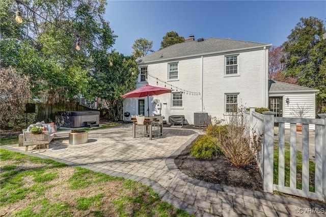 rear view of property with brick siding, a hot tub, central air condition unit, a fenced backyard, and a patio