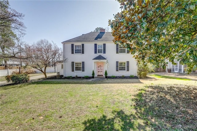 colonial home with a chimney, a front yard, and fence