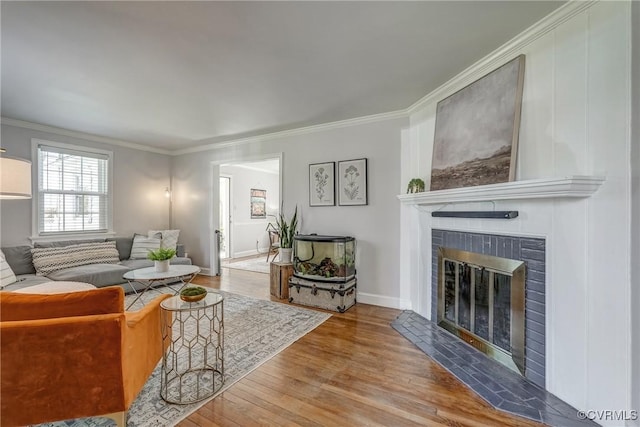 living area featuring ornamental molding, wood finished floors, baseboards, and a large fireplace