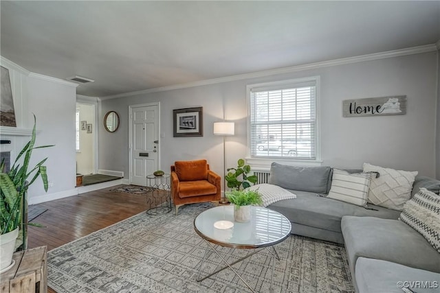 living area with wood finished floors, baseboards, visible vents, a fireplace, and ornamental molding