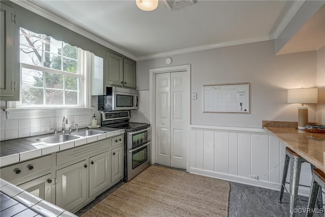 kitchen with tile countertops, stainless steel appliances, wainscoting, and crown molding