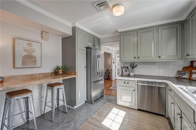 kitchen featuring visible vents, crown molding, a kitchen bar, decorative backsplash, and appliances with stainless steel finishes