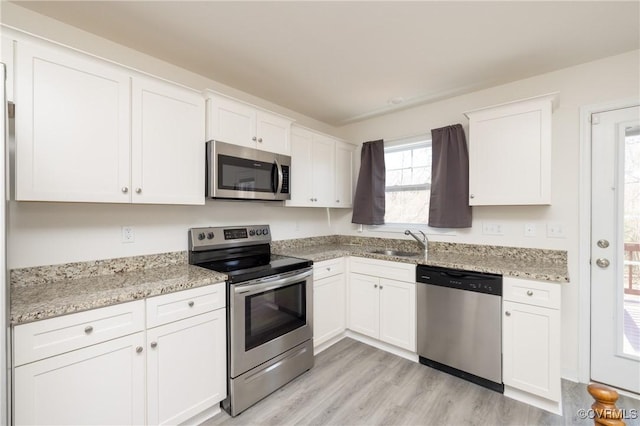 kitchen with light stone countertops, light wood finished floors, a sink, white cabinets, and appliances with stainless steel finishes