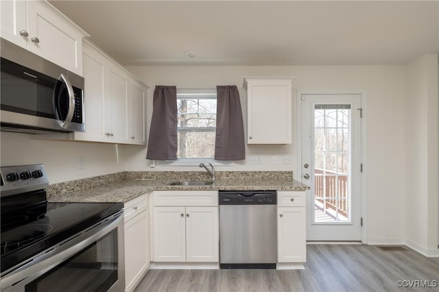 kitchen with light stone counters, a sink, white cabinets, appliances with stainless steel finishes, and light wood-type flooring