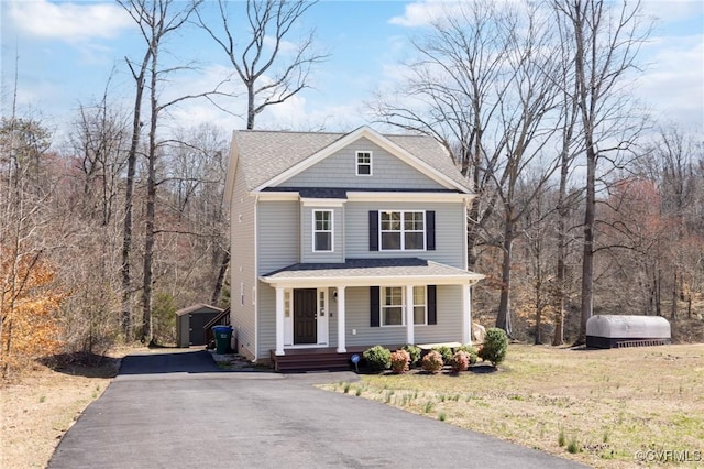 view of front of property featuring aphalt driveway, a wooded view, covered porch, and an outdoor structure