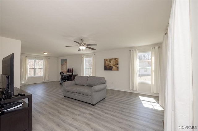 living area with light wood finished floors, baseboards, and a ceiling fan