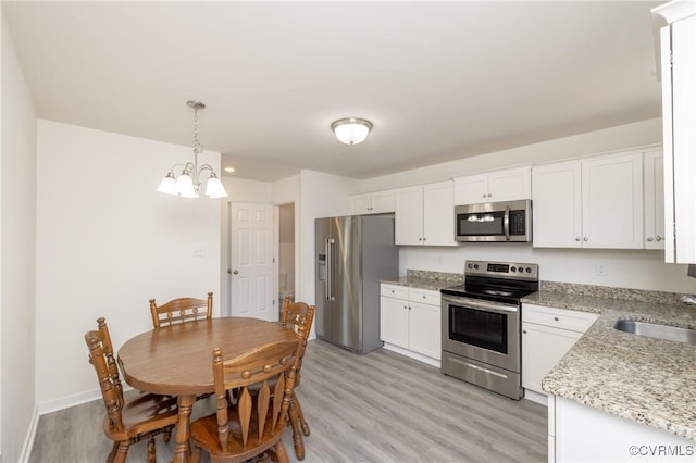 kitchen with a sink, decorative light fixtures, white cabinetry, stainless steel appliances, and light wood finished floors