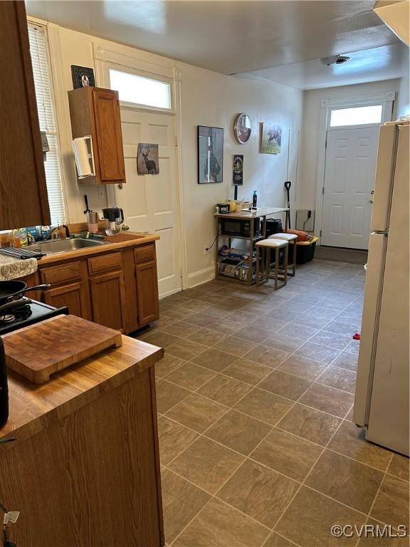 kitchen featuring a sink, black gas stove, freestanding refrigerator, butcher block counters, and brown cabinetry