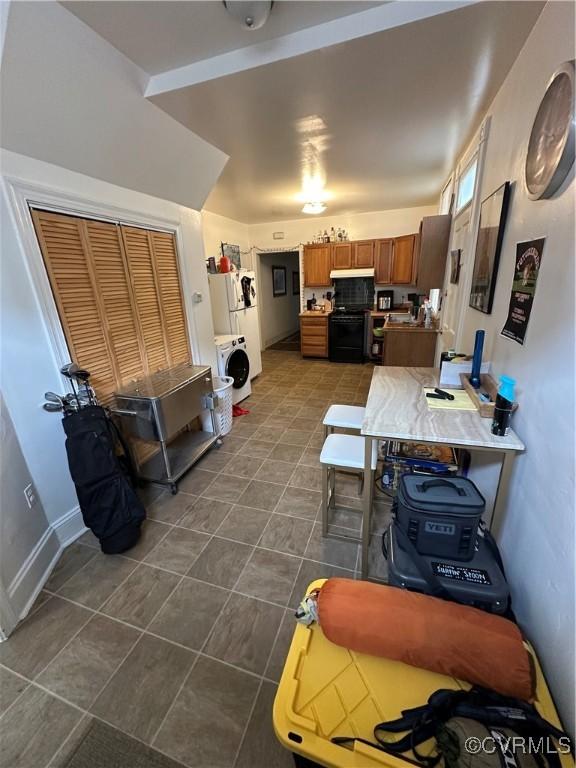 kitchen featuring dark tile patterned floors, black range, brown cabinetry, baseboards, and washer / dryer