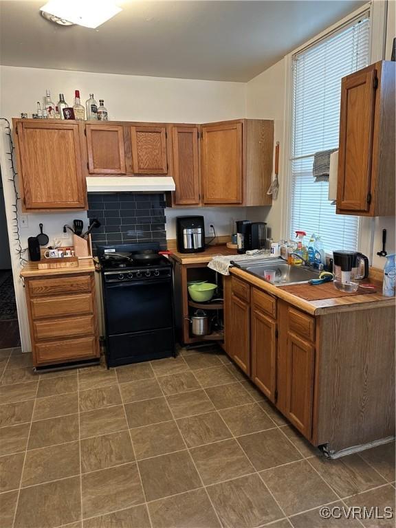 kitchen featuring gas stove, a sink, light countertops, under cabinet range hood, and brown cabinets