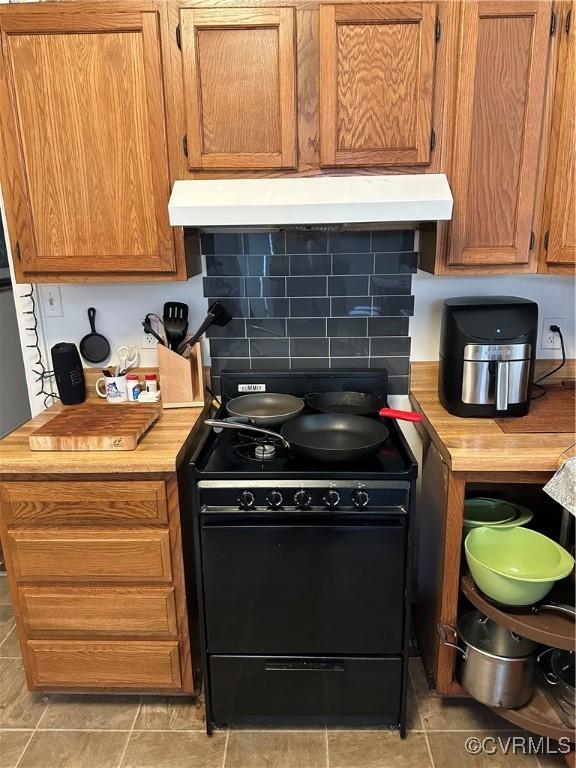 kitchen featuring decorative backsplash, ventilation hood, black range oven, and light countertops