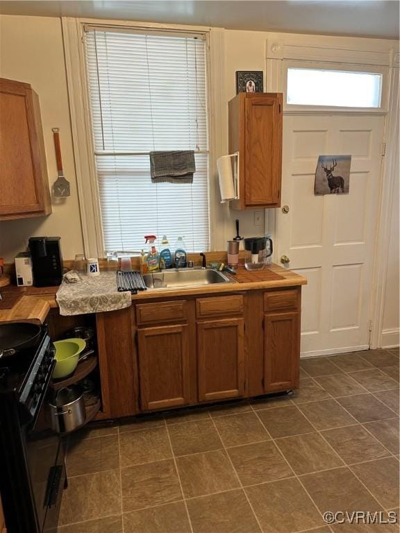 kitchen featuring electric range, dark tile patterned floors, a sink, brown cabinetry, and light countertops