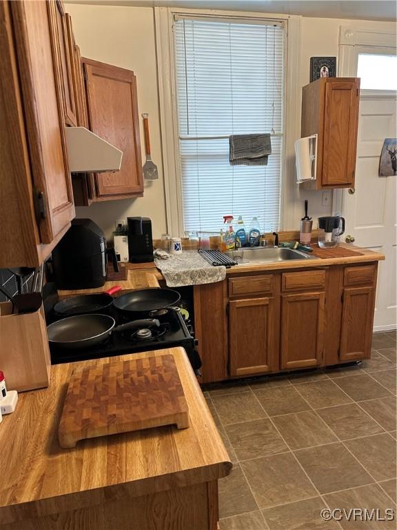 kitchen featuring ventilation hood, a sink, brown cabinetry, and gas stove