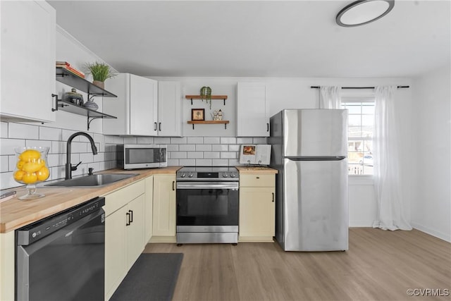 kitchen featuring butcher block countertops, light wood-style flooring, open shelves, a sink, and stainless steel appliances