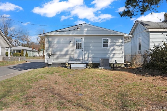 rear view of property with central AC unit, fence, entry steps, aphalt driveway, and a lawn